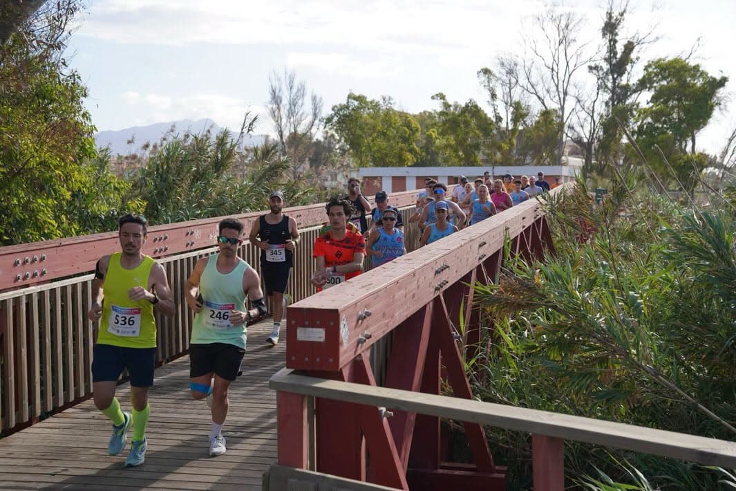 Corredores con dorsal cruzando una pasarela de madera del corredor litoral de Estepona
