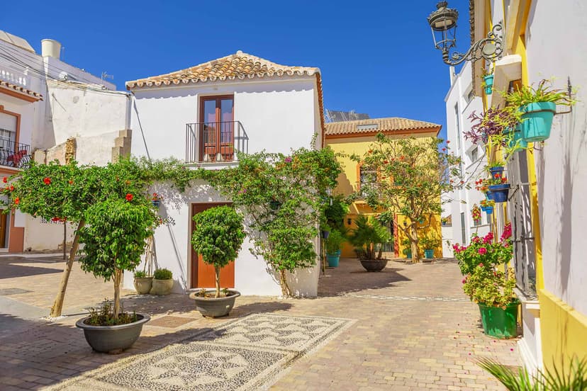 Rincón del casco de Estepona con suelo de canto rodado y árboles en macetas.