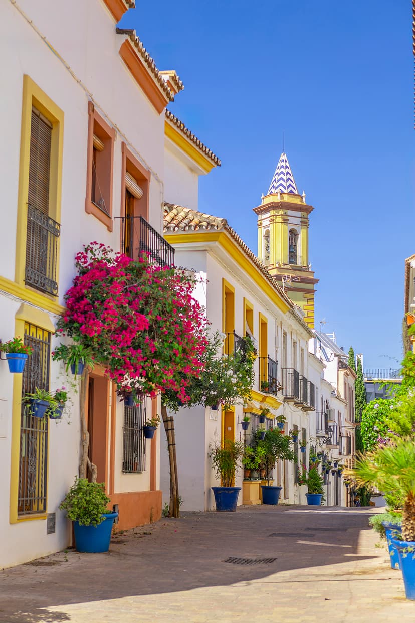 Calle con la torre de la Iglesia de los Remedios al fondo y buganvilla en primer plano, Estepona.